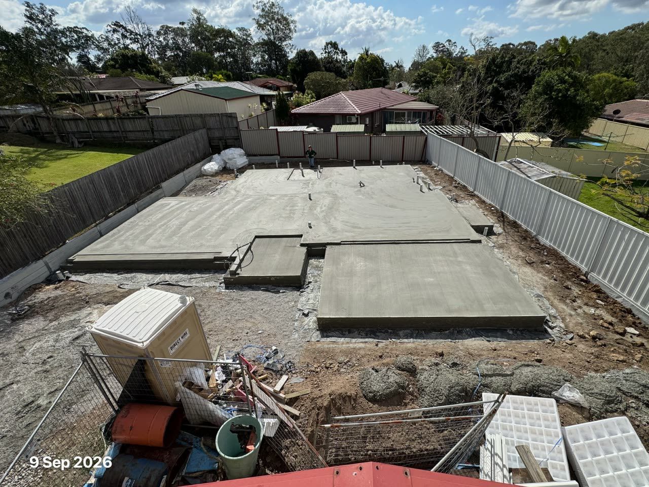 A freshly poured concrete slab in a fenced backyard, seen from a roof, with the date stamp 9 Sep 2026.