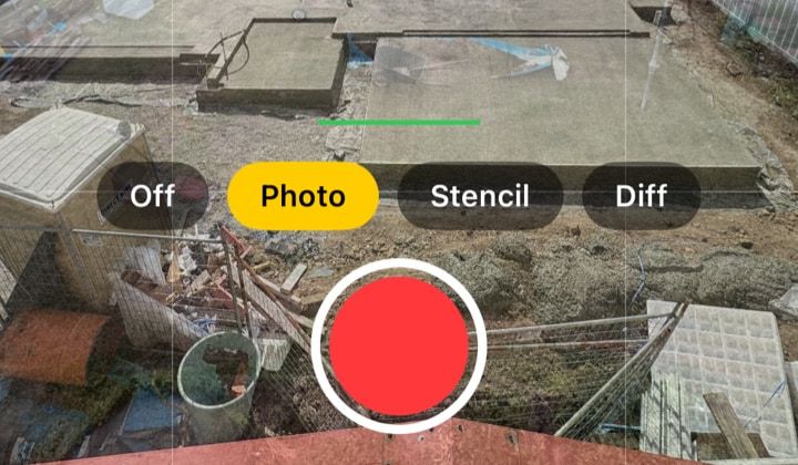 iPhone camera in moment mode: the Photo guide still selected, the key photo's wheelbarrow and tarp faint over the slab, and a red record button.